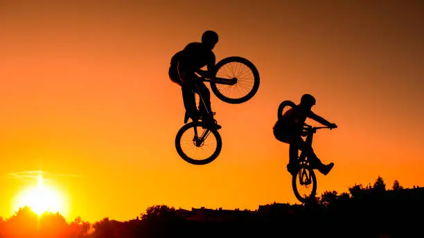 Shot of two mountain bikers jumping in sunset, copy space.
