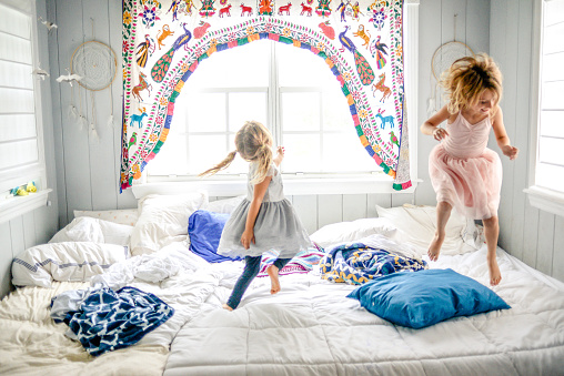 Two girls, sisters, friends, dance, play and jump on the bed in pretty outfits