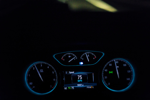 Bright modern digital dashboard display in a car speeding on an expressway at night. The speedometer indicates the vehicle is moving at 75 miles per hour.