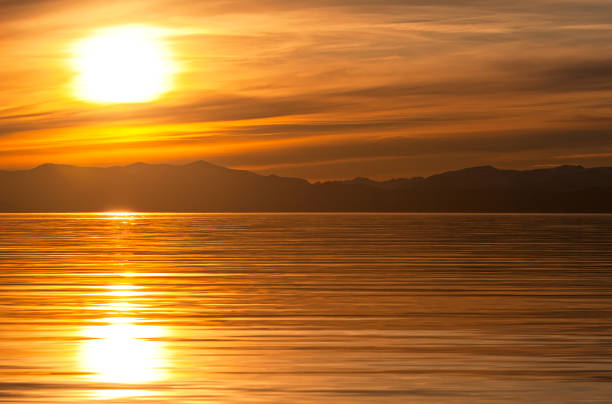 istock Golden sunset on the water with mountains in the background 874651400