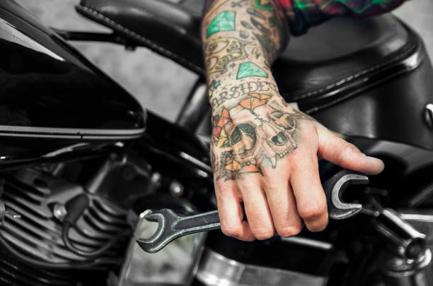 Closeup, tattooed man hand holding wrench making modifications to motorcycle , bike mechanic