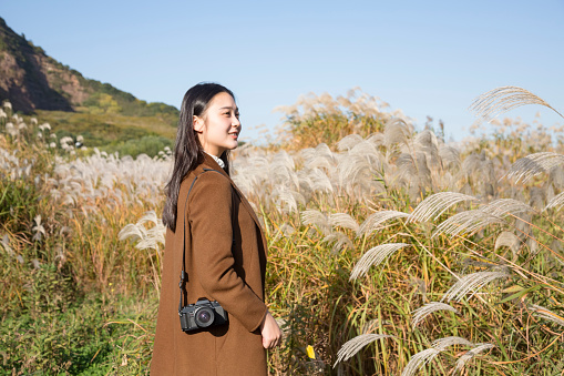 beautiful woman carrying camera walking through grassy field,autumn background.