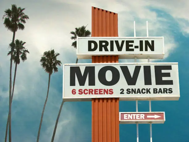 aged and worn drive in movie sign with palm trees