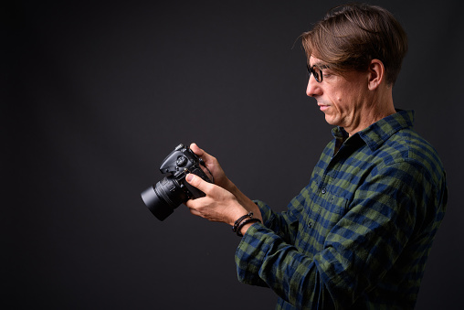 Studio shot of mature handsome Italian man wearing eyeglasses against gray background