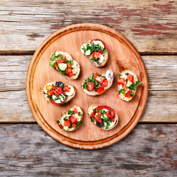 bruschetta italiana con tomates asados, queso mozzarella y hierbas sobre una tabla de cortar - bruschetta cutting board italy olive oil fotografías e imágenes de stock