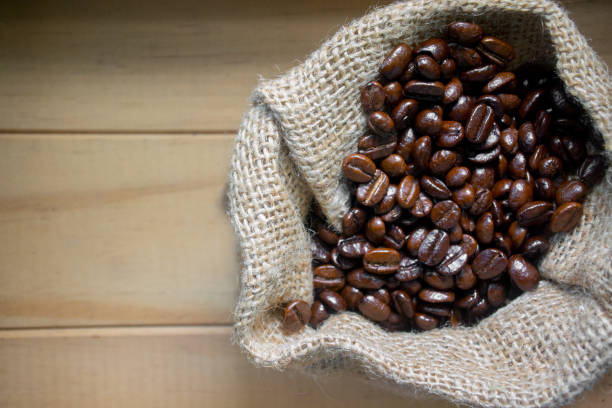 istock Roasted coffee beans in a small canvas bag - on a wooden table background. 874727866