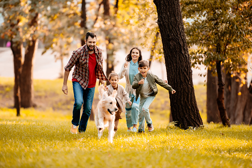 Happy family with two children running after a dog together in autumn park