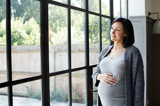 Shot of a pregnant woman looking out the window at home