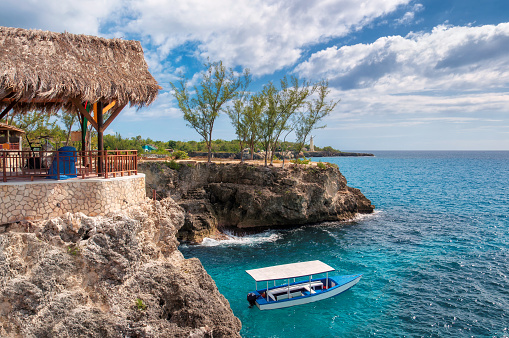 Negril, Jamaica, Caribbean rocky beach with turquoise water, tourists boat and lighthouse.