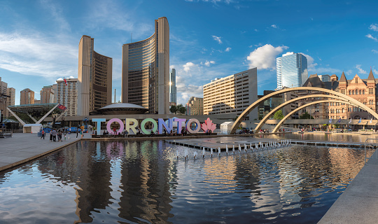 Toronto City Hall and Nathan Phillips Square at sunset on June 28, 2017 in Toronto, Canada. people walk by Toronto sign at sunset.