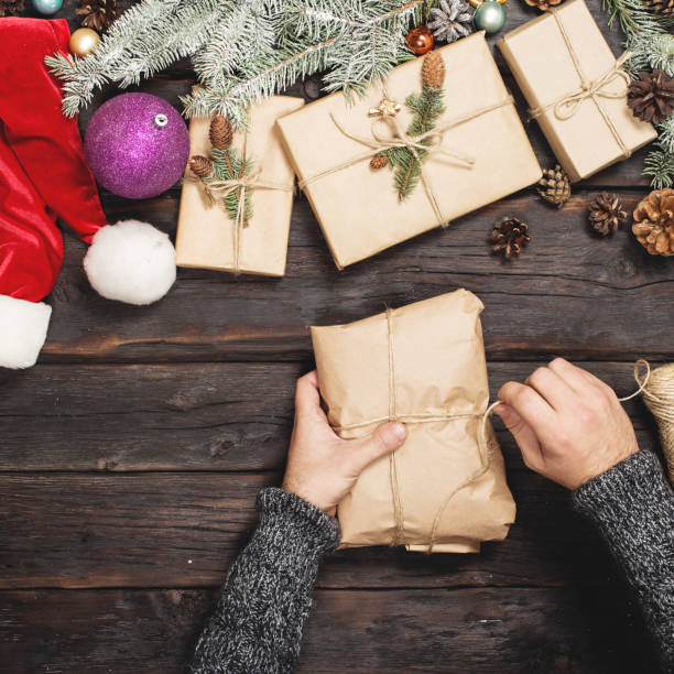 istock Man wraps Christmas gift on wooden table, top view 874754562