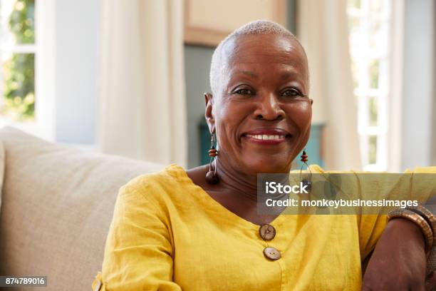 Portrait Of Smiling Senior Woman Sitting On Sofa At Home Stock Photo - Download Image Now