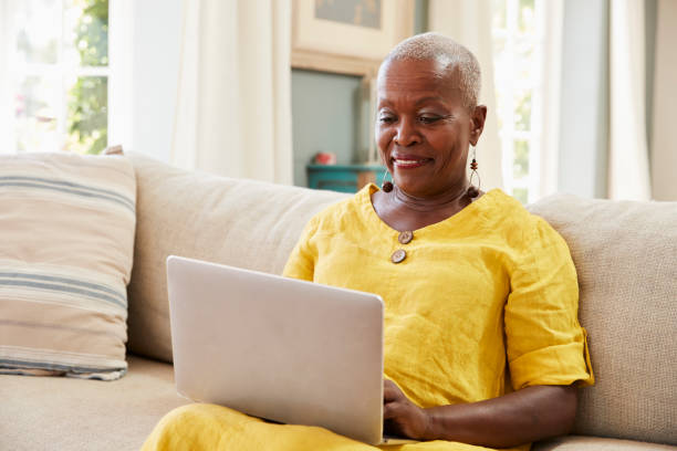 donna anziana seduta sul divano usando laptop a casa insieme - senior adult computer senior women women foto e immagini stock