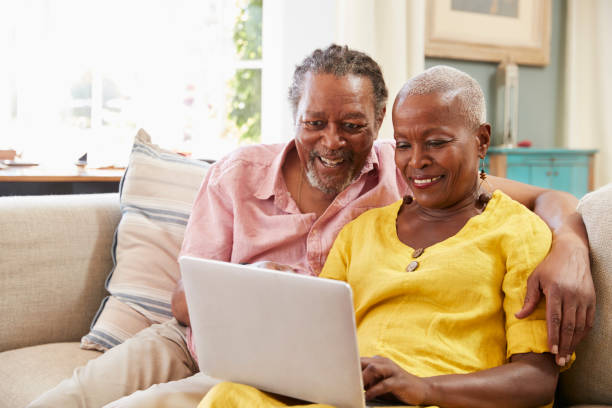 coppia senior seduta sul divano usando laptop a casa insieme - computer old men laptop foto e immagini stock