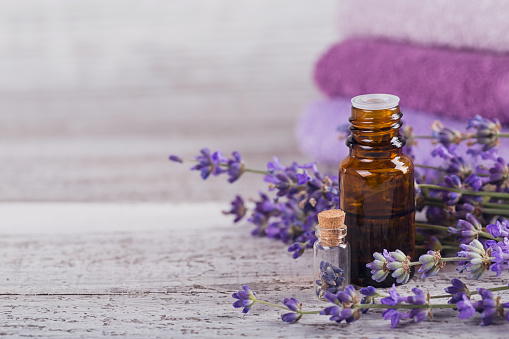 Bottle of essential oil and fresh lavender flowers on a white wooden background. Aromatherapy, spa and wellness concept