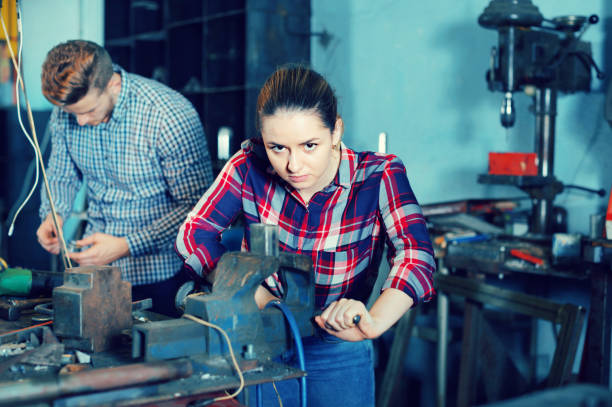 istock Girl worker is standing near vise equipment in workshop. 874801112