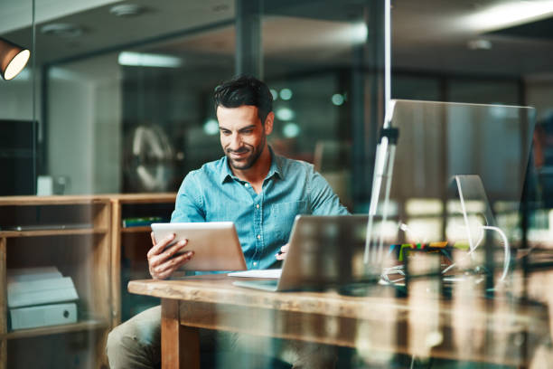 The digital worker gets things done Shot of a young businessman using a digital tablet at his desk in a modern office happy entrepreneur stock pictures, royalty-free photos & images