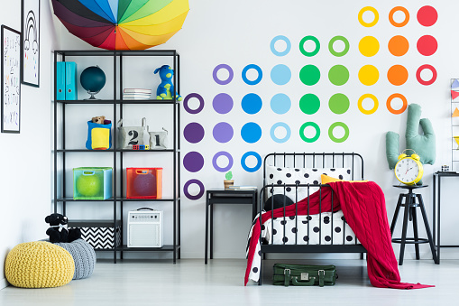 Colorful wall sticker in child's room with yellow clock on black stool and pouf on floor