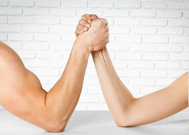 Man and woman doing arm wrestling over wall background
