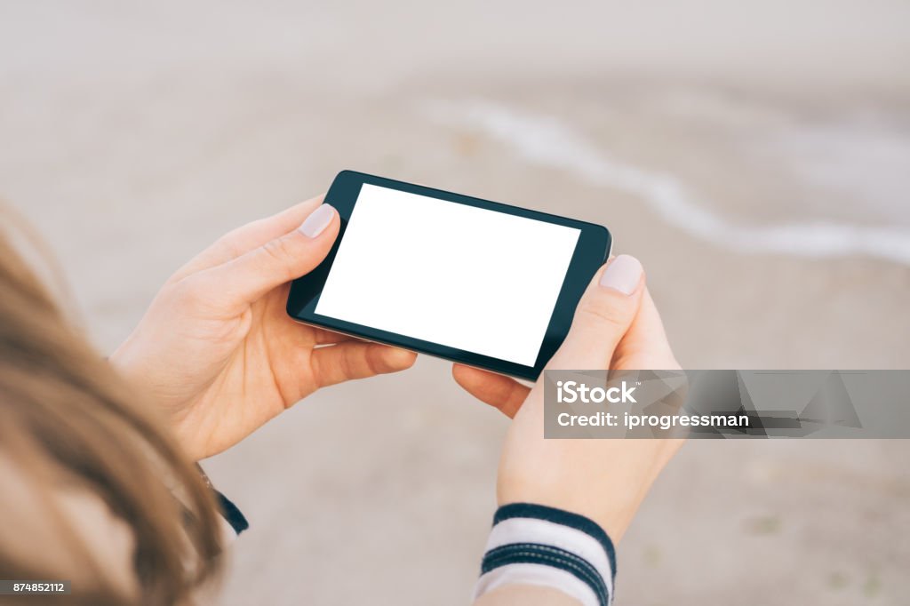 Smart phone with a white screen in female hands Smart phone with a white screen in female hands on a beach, close-up Human Hand Stock Photo