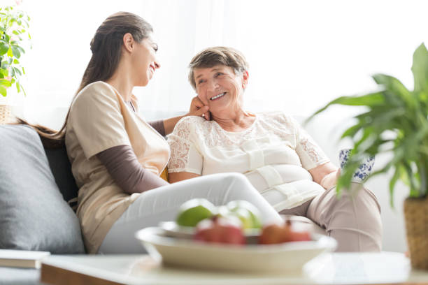 Woman talking with elderly mother Woman talking with happy elderly mother while sitting on sofa at home during meeting alzheimer patient stock pictures, royalty-free photos & images