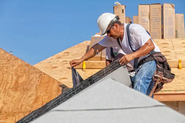 Photo of Roofer tears off protective cover of underlayment on a new roof