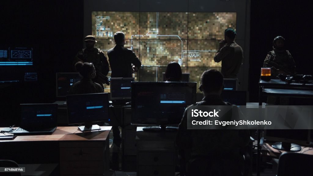 Group of people in dark room launching a missle Group of soldiers or spies in dark room with large monitors and advanced satellite communication technology launching a missle. Includes flashing yellow light. Military Stock Photo
