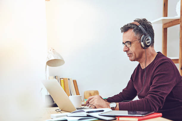 Some music to get the work going Shot of a mature man listening to music while using a laptop at home one mature man only audio stock pictures, royalty-free photos & images