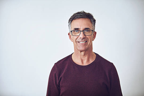 He has a casual demeanour Studio portrait of a handsome mature man posing against a grey background real life photos stock pictures, royalty-free photos & images
