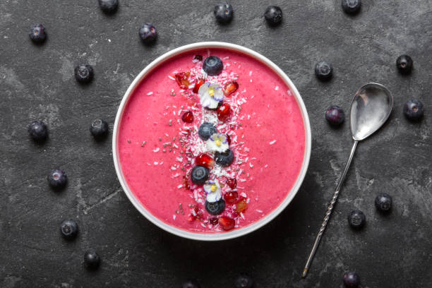 istock Strawberry and beetroot smoothie bowl topped with blueberries, pomegranate seeds, eatable pancy flowers and shredded coconut on a black concrete background. Top view center. 874875046