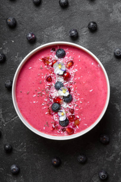 istock Strawberry and beetroot smoothie bowl topped with blueberries, pomegranate seeds, eatable pancy flowers and shredded coconut on a black concrete background. Top view center. 874875074