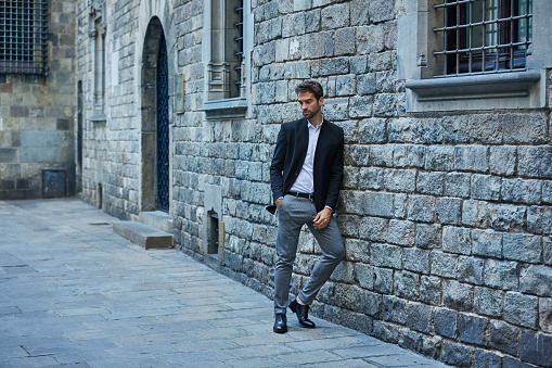Full length shot of a handsome young businessman standing against a brick wall in an urban alleyway