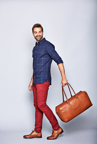 Studio shot of a handsome young man carrying a suitcase against a grey background