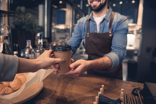 Close up female hand taking cup of hot coffee from barista in confectionary shop. Purchase concept