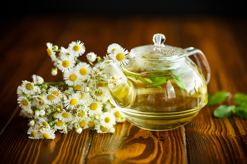 Glass teapot with chamomile tea on a wooden table