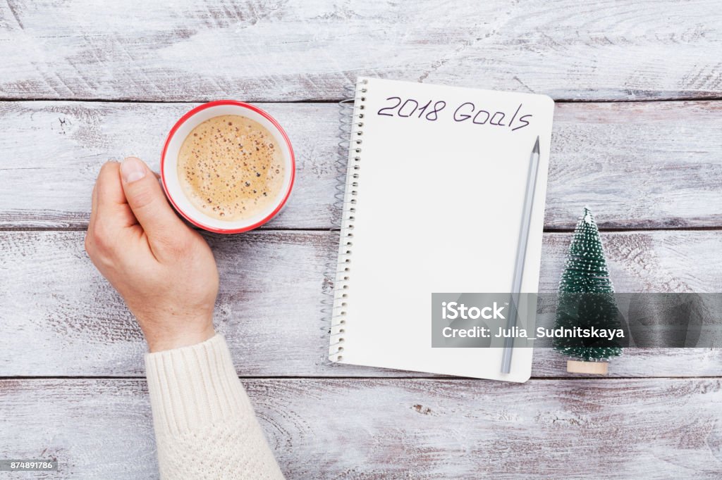 Taza de café y notebook con goles de asimiento de la mano masculina para 2018. Planificación y la motivación para el concepto de año nuevo. - Foto de stock de 2018 libre de derechos