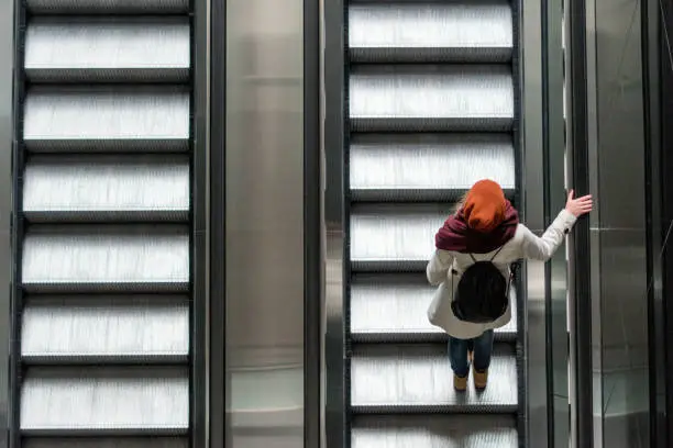 View from above on a young fashionable woman standing on the escalator stairs
