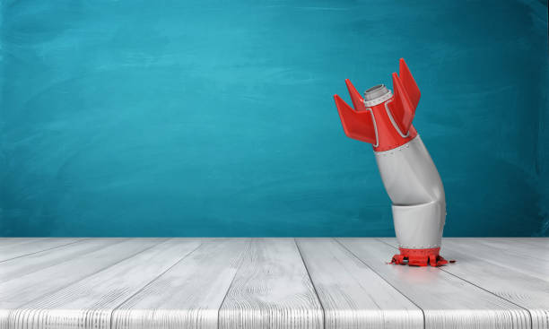 3d rendering of a red and silver realistic model of a retro rocket stands crashed into a wooden desk on a blue background. - failure imagens e fotografias de stock