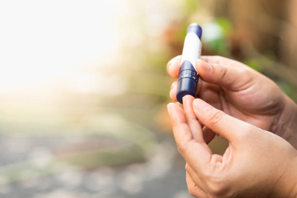 cerca de las manos de mujer con lanceta en el dedo para comprobar el nivel de azúcar en la sangre por medidor de glucosa utilizando como medicina, diabetes, glucemia, cuidado de la salud y personas concepto. - blood sugar test fotografías e imágenes de stock