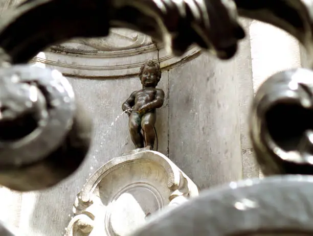 Photo of Bronze Sculpture of Manneken Pis as View Through the Iron Fence, a Small but Famous Landmark of Brussels of Belgium