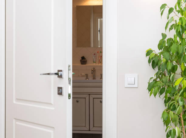 istock Ajar white door in a dark bathroom. Series switch on a light gray wall 874921982