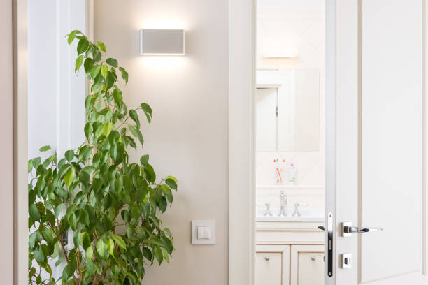 istock Ajar white door in the bright bathroom. Series switch and modern wall lamp on light gray wall 874921990