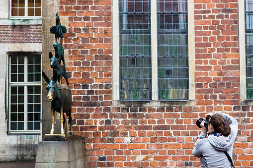 Bremen: tourist takes photo of bronze statue of Bremen Town Musicians in Bremen city in autumn. The statue was erected in 1953 by sculptor Gerhard Marcks