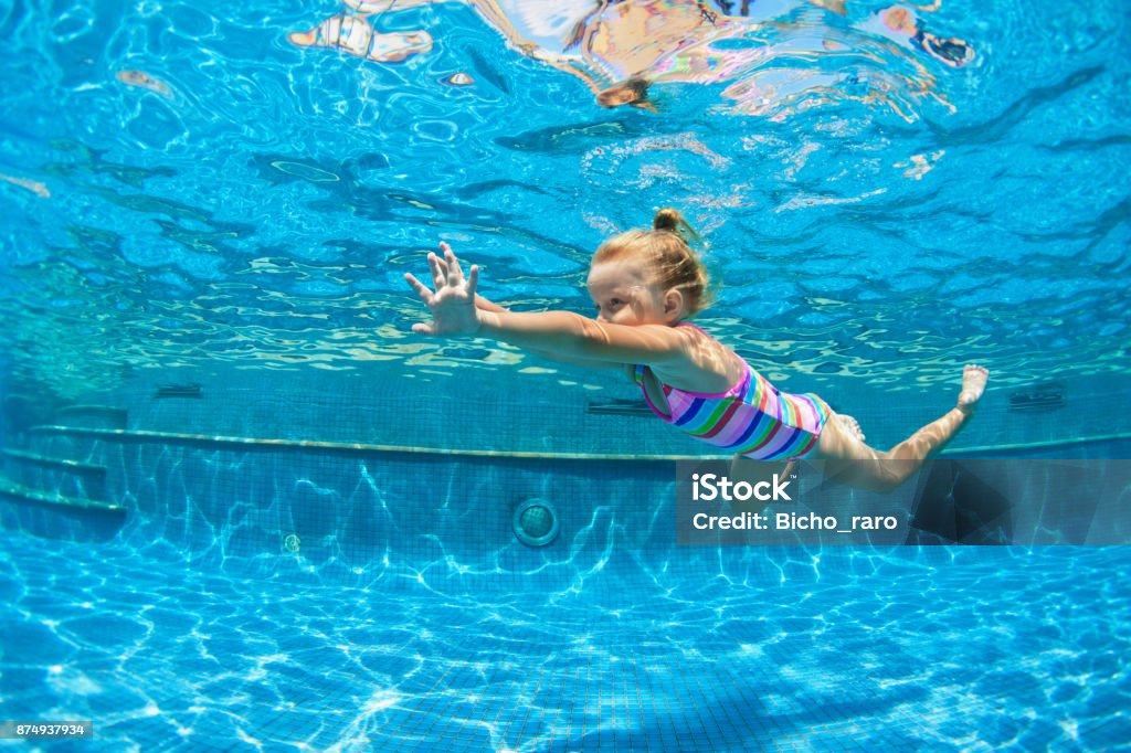 Child jump underwater into swimming pool Funny portrait of child learn swimming, diving in blue pool with fun - jumping deep down underwater with splashes. Healthy family lifestyle, kids water sports activity, swimming lesson with parents. Child Stock Photo