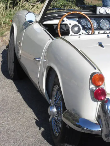 Photo of Left side of an old british classic car . Particular view of left tail light, dashboard and shiny chrome bumper . The car is a Triumph TR3 model produced between 1955 and 1962