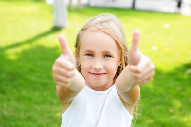 счастливая маленькая девочка показывает большие пальцы на открытом воздухе в летний день - hand sign human hand ok sign grass стоковые фото и изображения