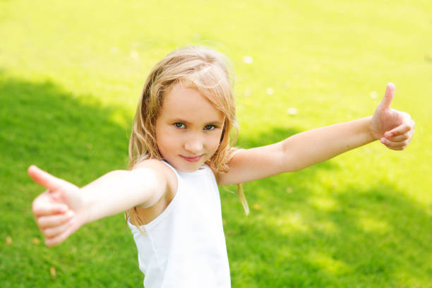 счастливая маленькая девочка показывает большие пальцы на открытом воздухе в летний день - hand sign human hand ok sign grass стоковые фото и изображения