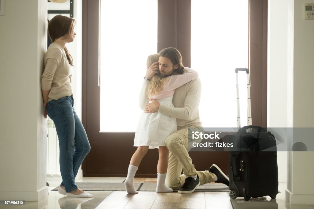 Sad father hugging little daughter before leaving for long trip Sad father hugging little daughter before leaving for long business trip, upset dad embracing crying girl saying goodbye to daddy at home in hall with baggage, family separation, good bye, farewell Leaving Stock Photo