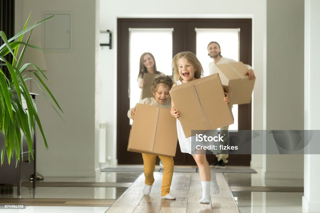 Excited kids running holding boxes, family moving in new house Happy family with kids bought new home, excited children funny girl and boy holding boxes running into big modern house, helping parents with belongings, moving day concept, mortgage and relocation Home Ownership Stock Photo