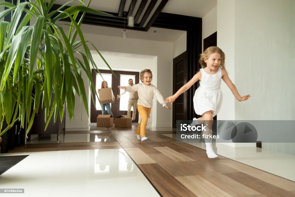 Excited children running into house, moving day in new home Happy young family with cardboard boxes in new home at moving day concept, excited children running into big modern own house hallway, parents with belongings at background, mortgage loan, relocation Child Stock Photo